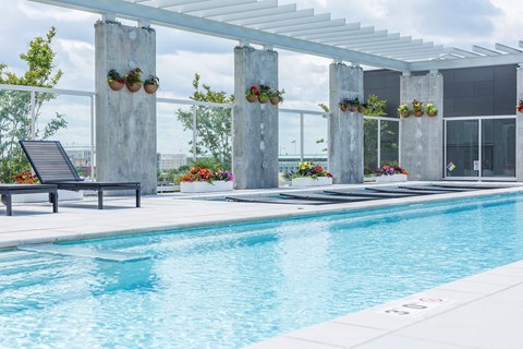Luxury community swimming pool area surrounded by architectural concrete pillars and vibrant hanging flower baskets.