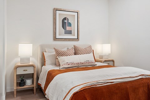 A bedroom with a bed, pillows, and a nightstand with a lamp.