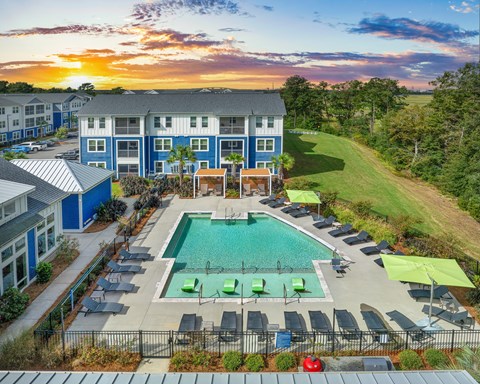 A sunset view of a pool area with lounge chairs and umbrellas.