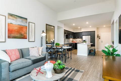 A modern living room with a grey couch and a dining area in the background.