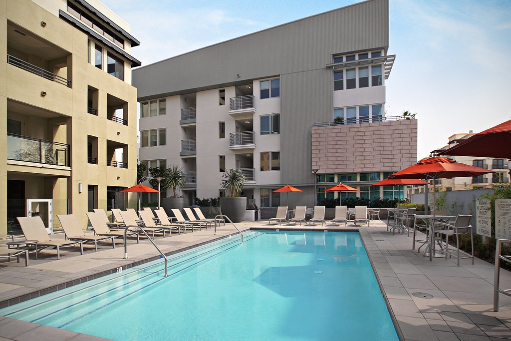 a swimming pool with chaise lounge chairs and umbrellas in front of a building