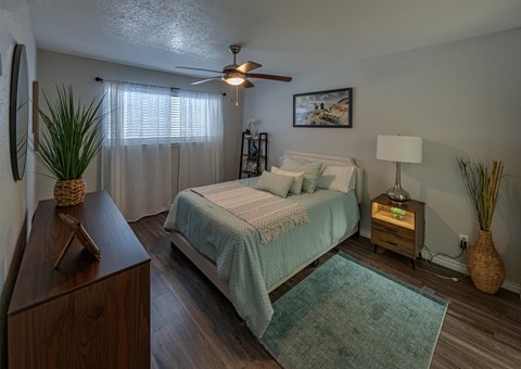 A bedroom with a bed, nightstand, and a plant. Un dormitorio con una cama, una mesita de noche y una planta.