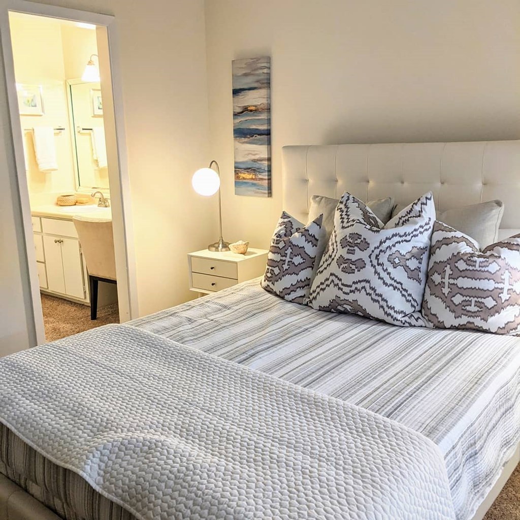 A bed with a white headboard and striped comforter with a white lamp on the bedside table.