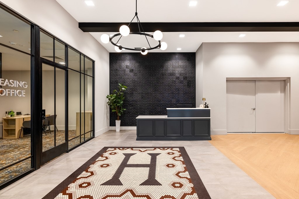 a lobby with a reception desk and a rug with a h on the floor