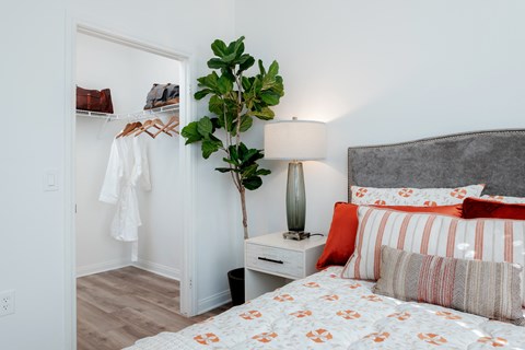 A bedroom with a bed, nightstand, and a plant.