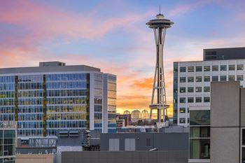 The Space Needle stands tall in front of a building with a sunset sky in the background.