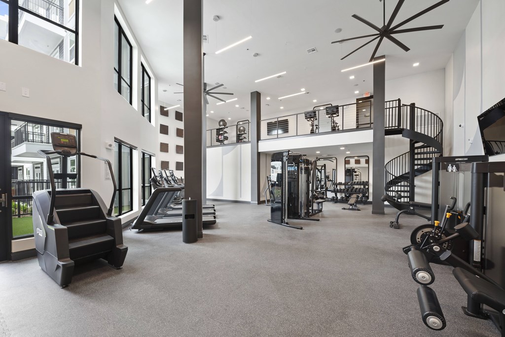 A spacious gym with a variety of equipment including treadmills, weight machines, and a spiral staircase.