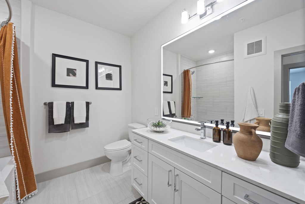 A bathroom with a toilet, sink, mirror, and two framed pictures on the wall.