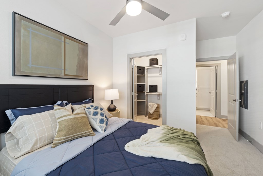 A bedroom with a bed, pillows, a ceiling fan, and a painting on the wall.