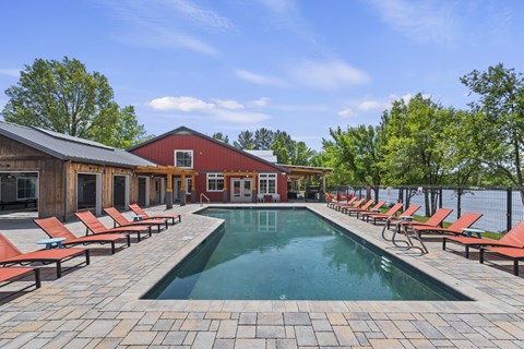 A pool surrounded by red lounge chairs and a wooden building.