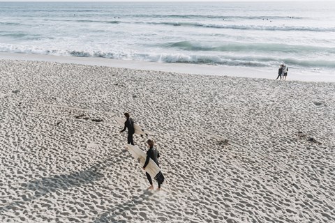 three surfers walking on the beach with their surfboards