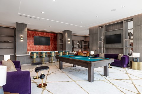 A billiard table is surrounded by purple chairs in a room with a red wall.