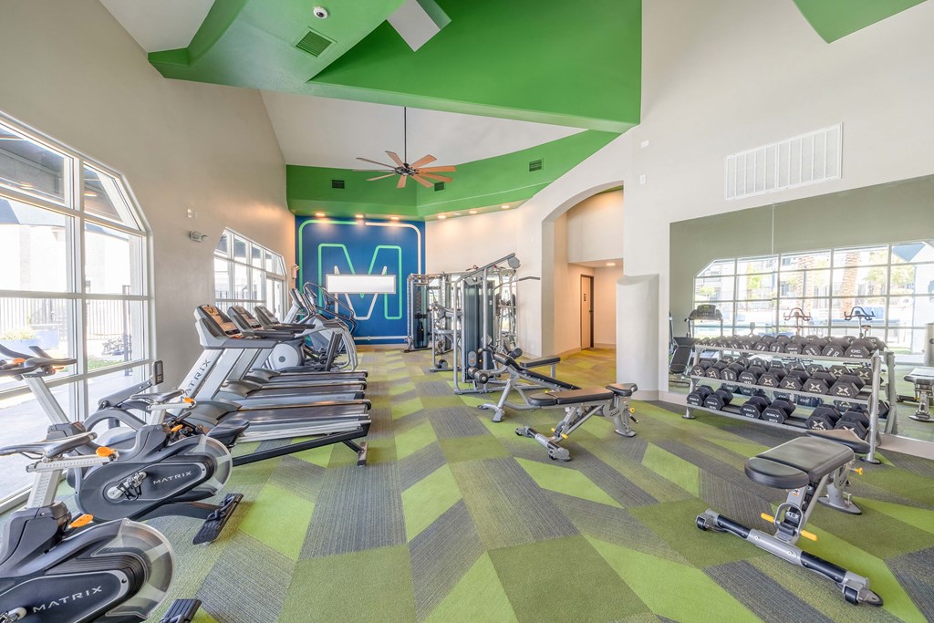 a spacious fitness center with cardio equipment and windows