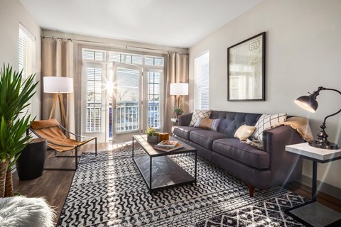A living room with a purple couch, a coffee table, and a large window with curtains.