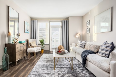 A living room with a white couch, a wooden dresser, a chair, a coffee table, and a rug.