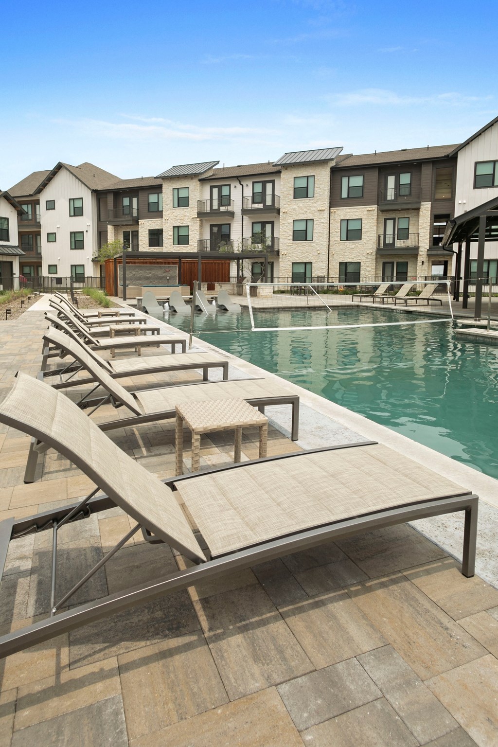 a pool with a row of wooden lounge chairs in front of an apartment building