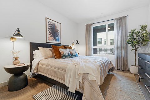 A bedroom with a bed, nightstand, and a plant.