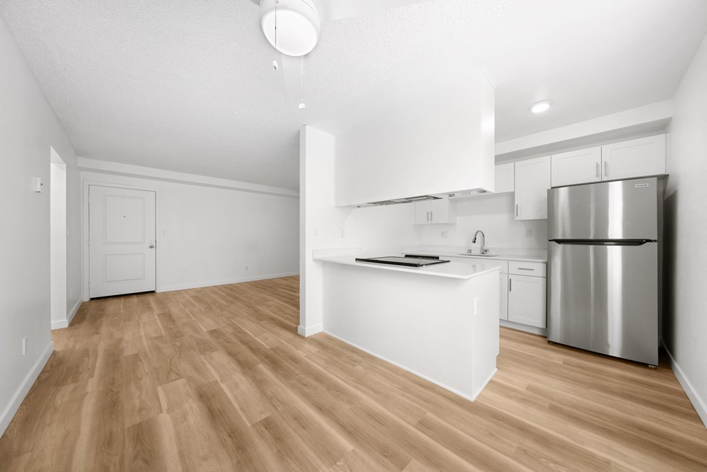 an empty living room with a kitchen with a stainless steel refrigerator