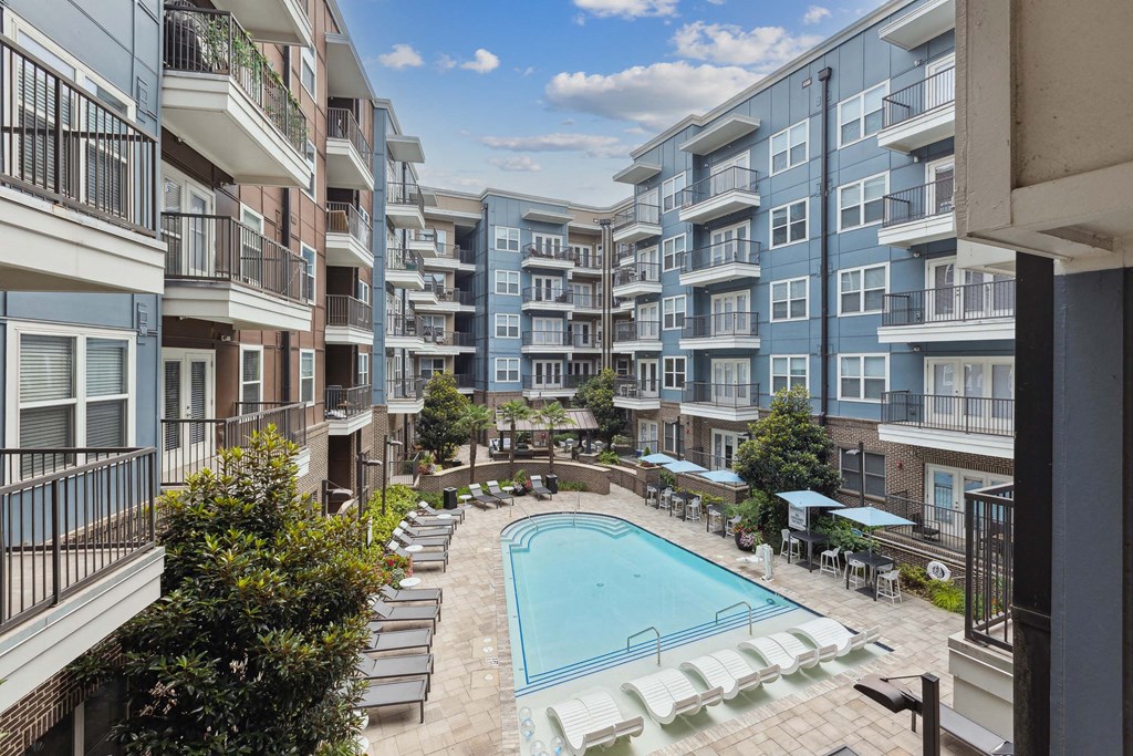 an outdoor pool with lounge chairs and umbrellas in front of an apartment building