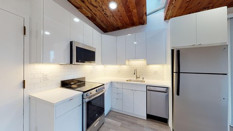 A modern kitchen with white cabinets and a wooden ceiling.