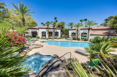 A pool surrounded by palm trees and a house in the background.