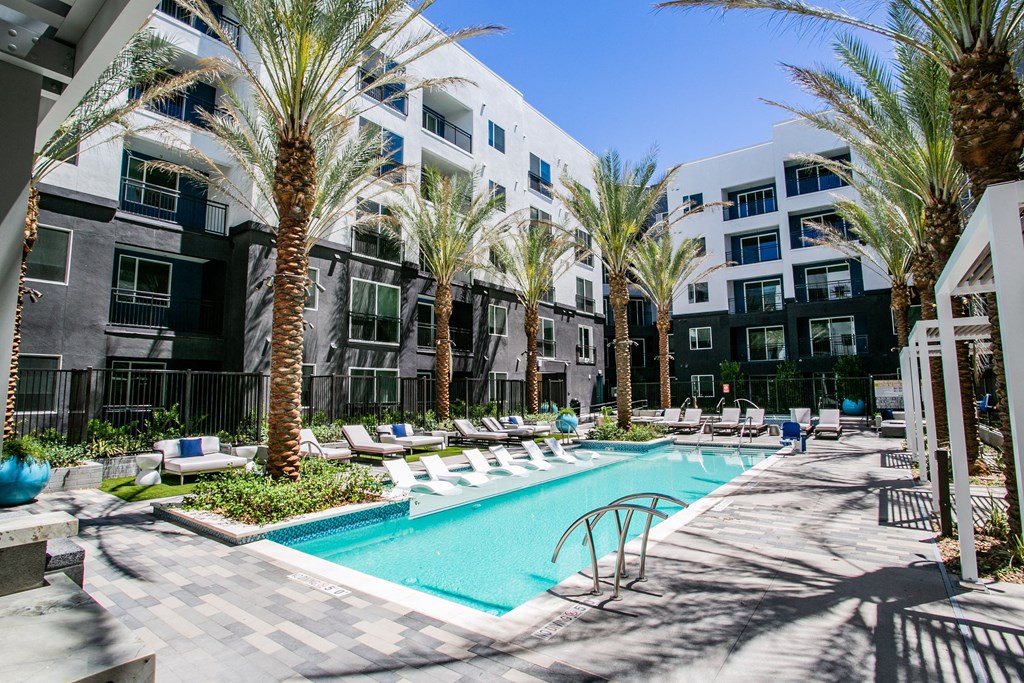 an outdoor swimming pool with chaise lounge chairs and palm trees in front of an apartment building