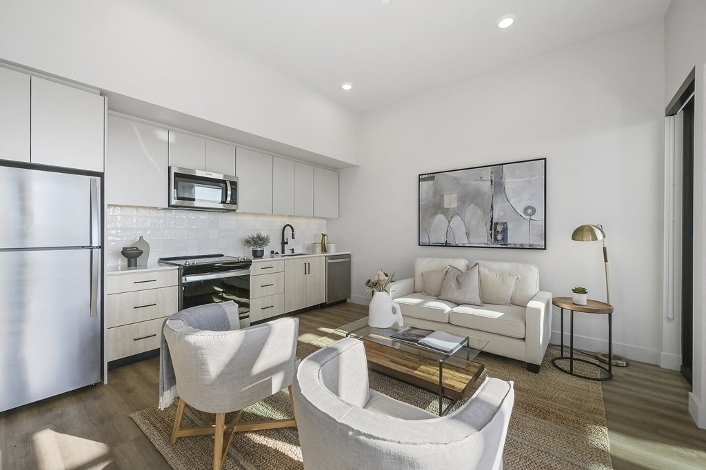 a living room with a couch and chairs and a kitchen with a refrigerator