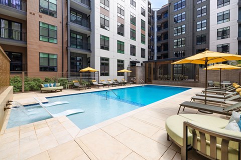 A pool surrounded by chairs and umbrellas in a courtyard.