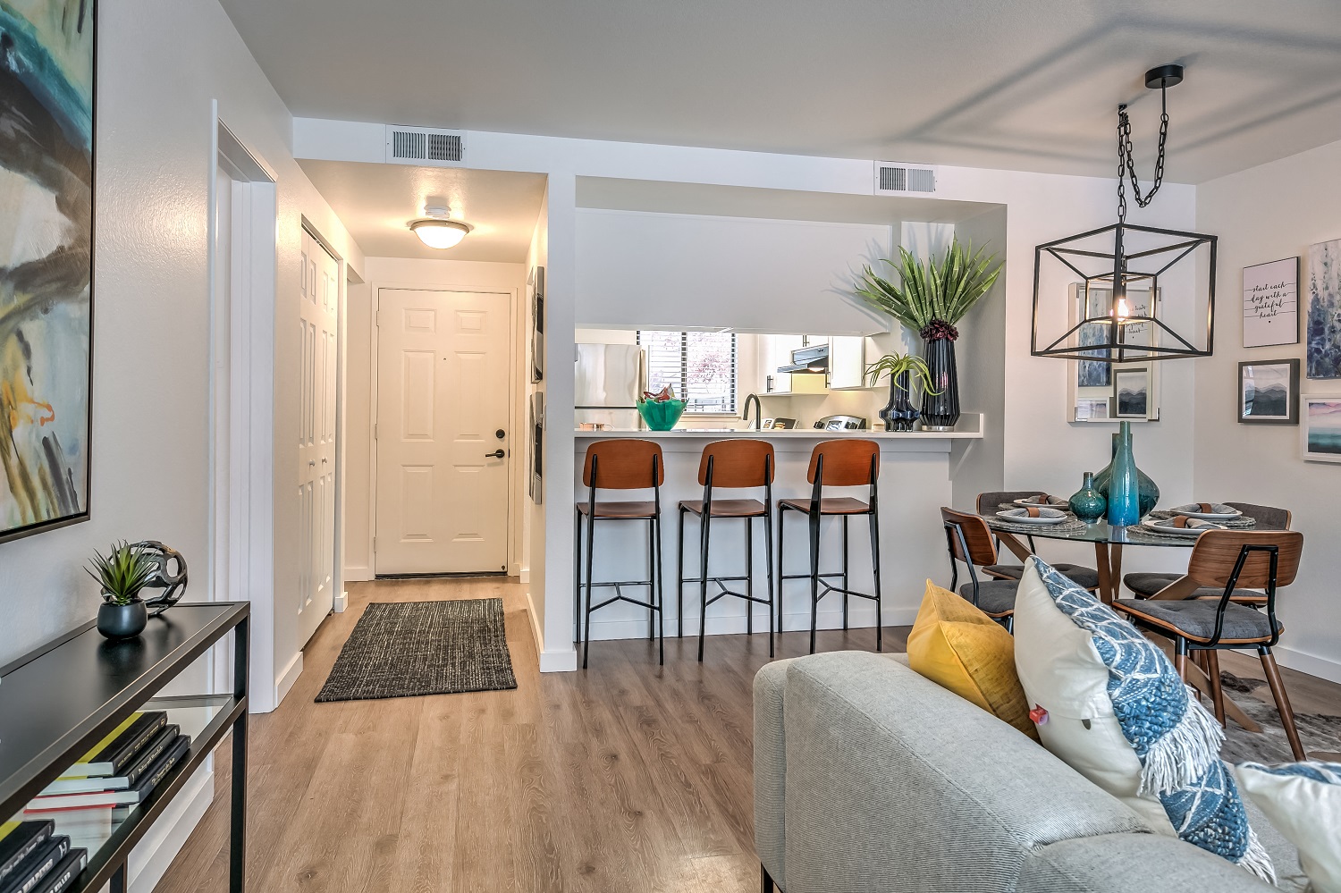 A living room with a grey couch and a bar area with stools.