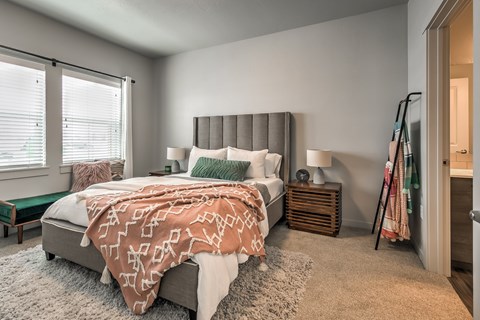 A bedroom with a bed covered in a patterned blanket and a wooden nightstand with a lamp.