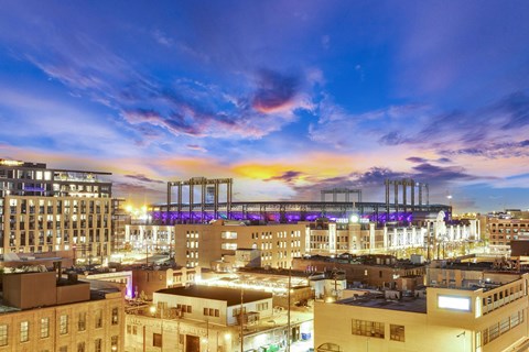 A cityscape at dusk with buildings and a bridge illuminated by artificial lights.