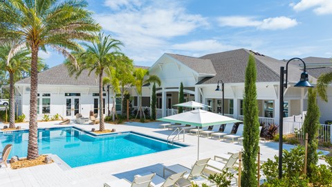 a large swimming pool with chairs and umbrellas in front of a house