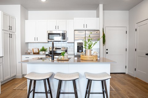 A kitchen with white cabinets and a white island with bar stools.