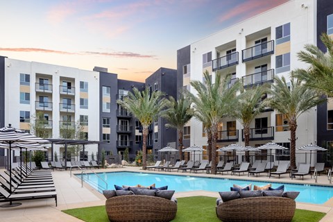 an outdoor pool with chairs and palm trees in front of an apartment building