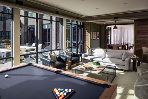 A pool table with a white ball on it is in the middle of a room with a couch and chairs.