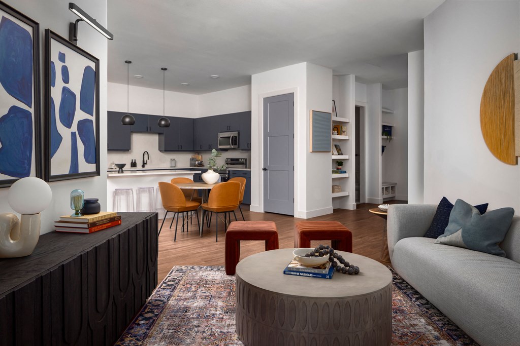 A modern living room with a grey couch, a round table, and a kitchen area in the background.