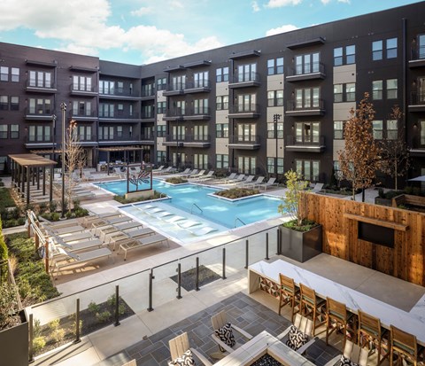 A large outdoor swimming pool surrounded by lounge chairs and buildings.
