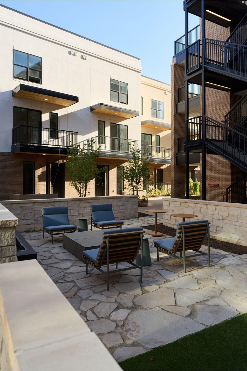 A patio with a table and chairs is in front of a building with a black spiral staircase.