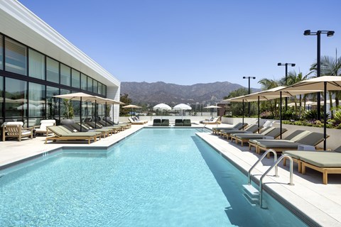 A large outdoor swimming pool with sun loungers and a mountain in the background.