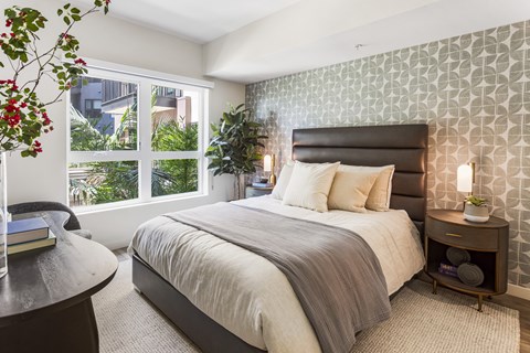 A bedroom with a large bed and a window overlooking a garden.