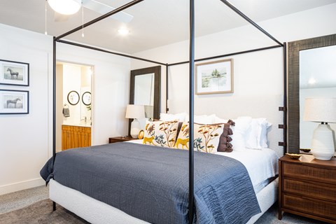 A bedroom with a four poster bed and a nightstand with a lamp.
