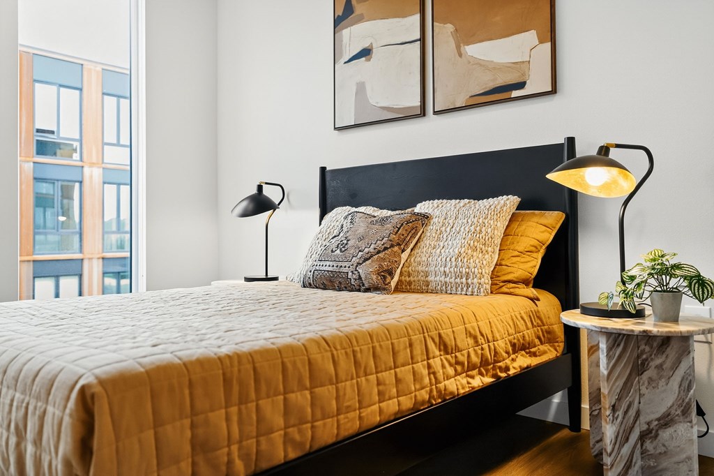 A bed with a yellow cover and a black headboard with two lamps on the side.