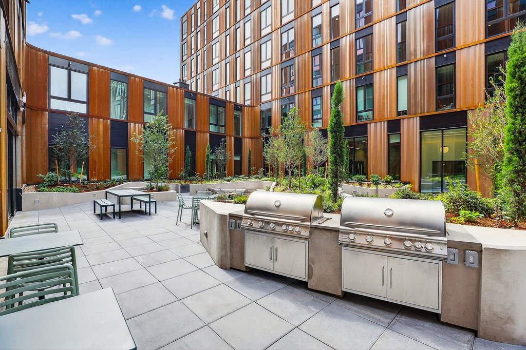 A courtyard with a grill and chairs is surrounded by a building.
