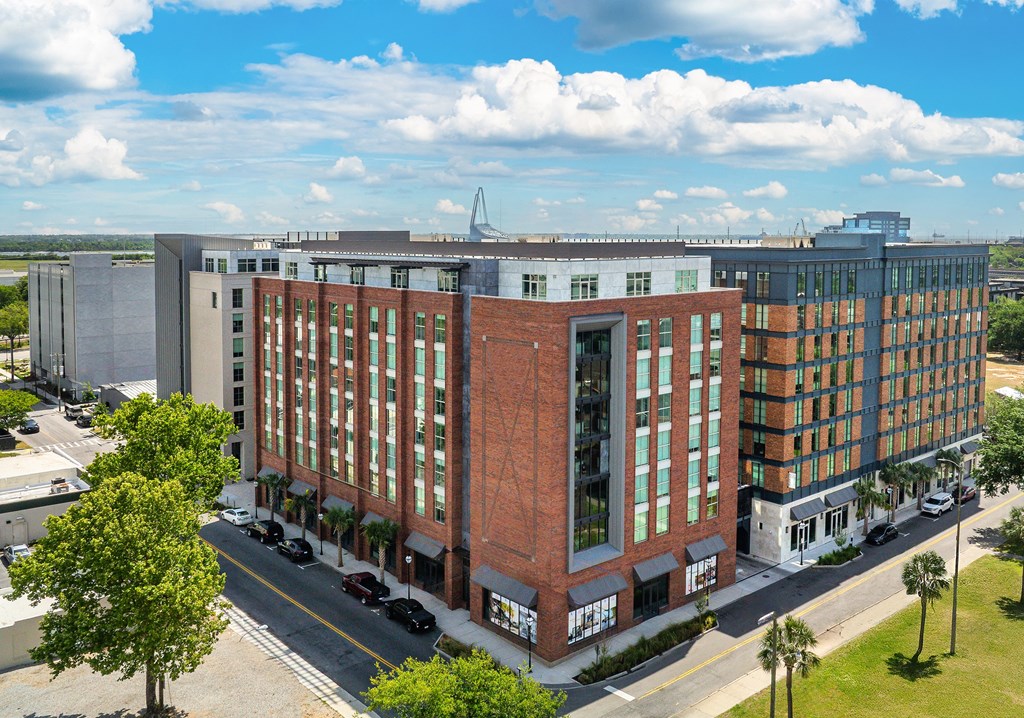 A large red brick building with a glass facade is surrounded by trees and other buildings.