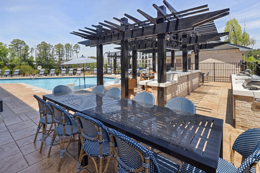 A black table with blue chairs is set up by a pool.