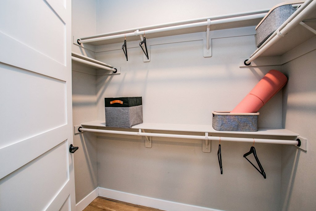 a walk in closet with white shelves and a white rail with black hangers