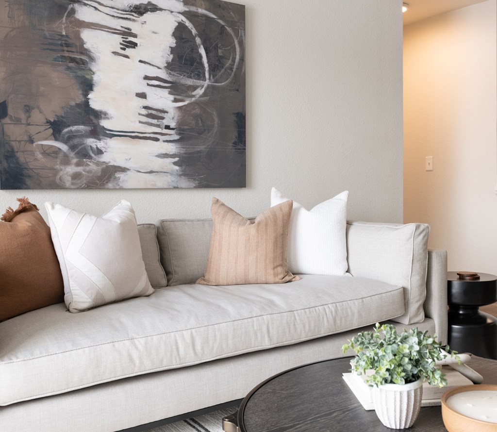 A living room with a white couch and a large abstract painting above it.