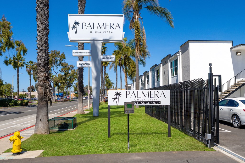 A sign for Palmera Chula Vista stands in front of a black fence.