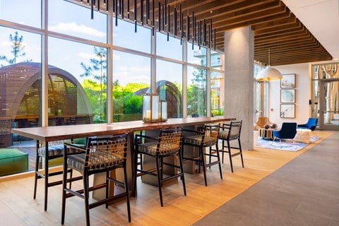 Resident lounge area featuring a modern breakfast bar with high chairs next to a large window overlooking the community.
