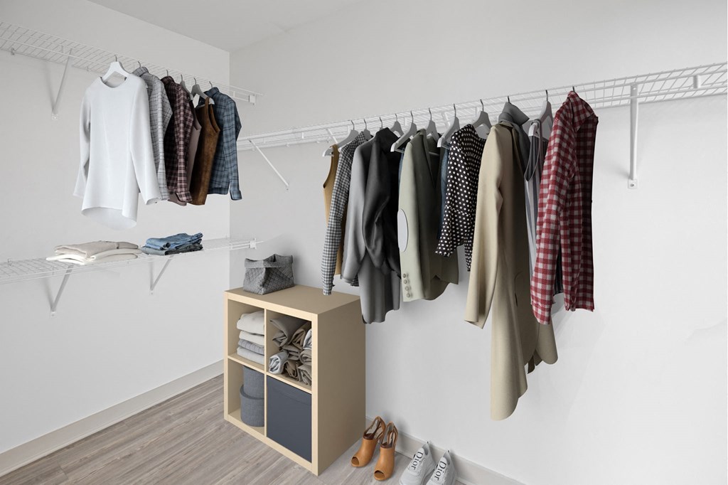 a walk in closet with clothes hanging on the wall and a small cabinet on the floor